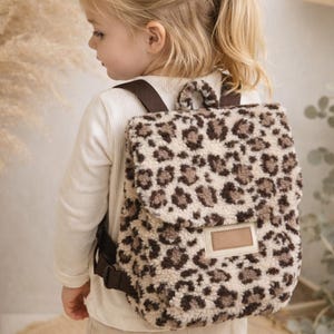 Kinderrucksack „Leo Style“ – Teddyplüsch - inklusive Namen auf einem Lederpatch -  Kuschelrucksack - Kita - Krippe- Geschenk ab 1 Jahr