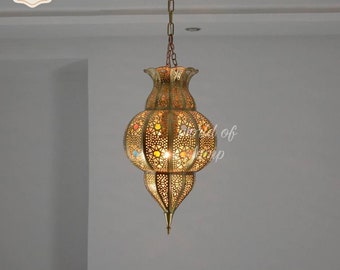 May include: A gold metal pendant light fixture with a decorative, intricate design. The light fixture is hanging from a chain and has a round, bulbous shape with a pointed bottom. The fixture has a stained glass design with colorful accents.