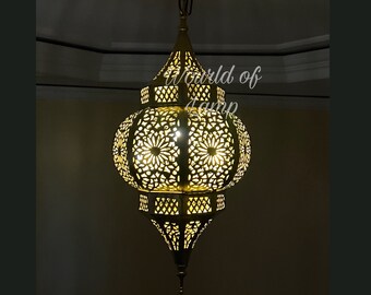 May include: A gold metal Moroccan pendant light with intricate cut-out designs. The light is hanging from a chain and is illuminated, casting a warm glow.