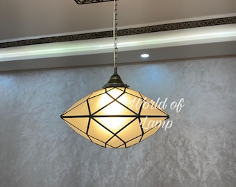 May include: A pendant lamp with a geometric design. The lamp has a cream-colored shade with black lines and a brass-colored frame. The lamp is suspended from a chain and is hanging from the ceiling. The text "World of Lamp" is in the upper left corner.