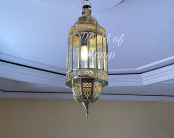 May include: A gold-toned metal pendant light fixture with a geometric design and clear glass panels. The light is hanging from a chain and is illuminated by a light bulb.
