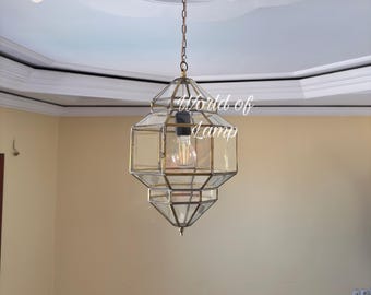 May include: A geometric pendant light fixture with a brass finish and clear glass panels. The light fixture hangs from a chain and has a visible lightbulb. The text "World of Lamp" is visible on the fixture.