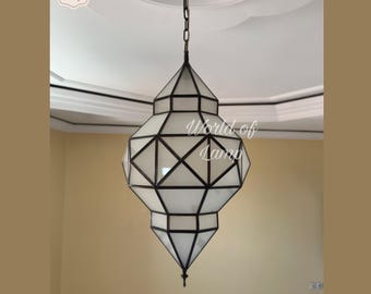 May include: Geometric pendant lamp with a white glass shade and black metal frame. The lamp is suspended from a chain. The text "World of Lamp" is visible on the lamp. The lamp's design is reminiscent of a lantern.