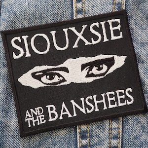 Könnte beinhalten: Schwarz-weiß gestickter Patch mit dem Text "Siouxsie and the Banshees" und einem stilisierten Bild von zwei Augen.