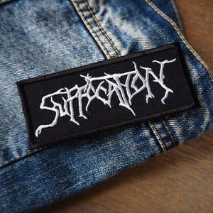 Può includere: Toppa ricamata in bianco e nero con la parola "Suffocation" in un font gotico.