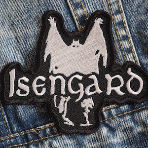 Pode incluir: Etiqueta bordada preta e branca com a palavra "Isengard" em letras brancas e uma silhueta branca de um morcego com uma criatura dentro.