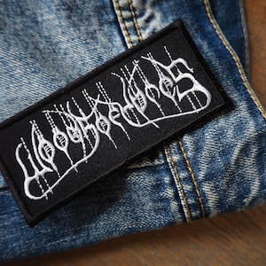 Puede incluir: Un parche bordado negro con el texto blanco "WOO DOO  WORM" sobre un fondo de mezclilla.