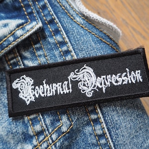 Puede incluir: Parche bordado negro con letras blancas que dicen "Nocturnal Depressor".