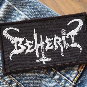 Puede incluir: Parche bordado en blanco y negro con el nombre de la banda "Behemoth" en una fuente estilizada. El parche presenta un pentagrama y cuernos.
