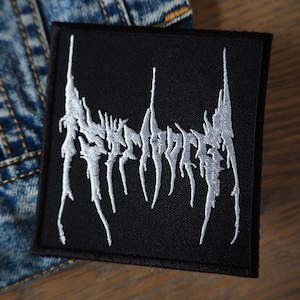 Puede incluir: Parche bordado negro con el texto blanco "Asymmetry" en una fuente estilizada.