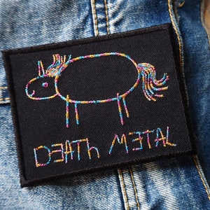 Puede incluir: Un parche negro con un dibujo bordado de colores de un unicornio y el texto "DEATH METAL" debajo.