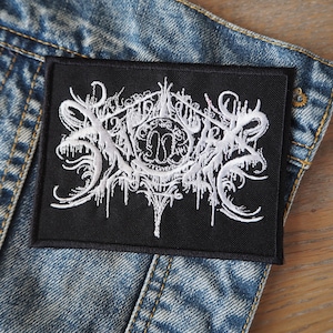 May include: White embroidered patch on a black background with the text "SLAUGHTER" in a gothic font.