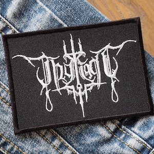 Puede incluir: Parche bordado negro con el texto blanco "Impiety" en una fuente gótica.