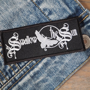 Puede incluir: Parche bordado negro con letras blancas que dicen "Swallow the Sun". El parche presenta un diseño de pájaro estilizado.