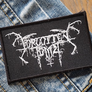 May include: Black and white embroidered patch with the text "Forgotten Tomb" in a stylized font.