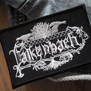 May include: Black embroidered patch with white lettering that reads "Darkthrone". The patch features a stylised design of a tree with branches and a bird.