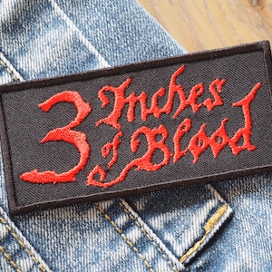 以下が含まれることがあります： 「3 Inches of Blood」と赤い文字で書かれた黒い刺繍パッチです。