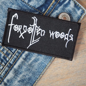 May include: Black embroidered patch with white lettering that reads "Forgotten Woods".