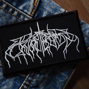 Può includere: Toppa ricamata bianca su sfondo nero con il testo "CRYPTS OF  " in un font stilizzato.