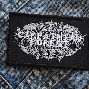 May include: White embroidered patch on a black background with the text "CREEPLY FOREST" in a gothic font.