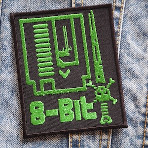 May include: A black, rectangular patch with green embroidered 8-bit graphic design. The patch features a stylized circuit board design and the words "8-BIT" in a bold, green font. The patch is set against a denim background.