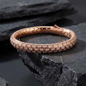 May include: Rose gold bracelet with a honeycomb design, encrusted with small, sparkling diamonds. The bracelet is displayed on a dark, textured surface, showcasing its intricate details and luxurious appeal. A beautiful piece of jewelry.