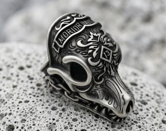 May include: A silver-toned metal ring shaped like a stylized animal skull with intricate engraved scrollwork, a banner featuring the text MORIOR INVICTUS, and a diamond-shaped emblem containing the number 13 on the side of the skull structure.