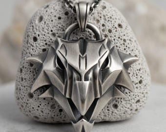 May include: A silver-toned metal pendant shaped like a stylized wolf head with sharp, angular features and a dark, brushed finish. The pendant is suspended from a matching silver-toned metal chain link, showcasing intricate geometric detailing.