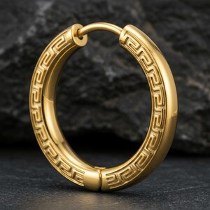 May include: A gold-toned hoop earring featuring a continuous engraved Greek key pattern along its outer surface. The circular earring has a smooth, polished finish and a hinged post mechanism that allows the hoop to open and close securely.