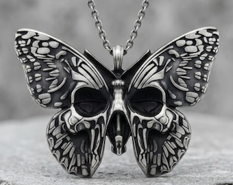 May include: A silver-toned metal pendant shaped like a butterfly with a skull motif integrated into the wing design. The pendant features dark oxidized recessed areas to highlight the intricate details and is suspended from a matching silver-toned chain.