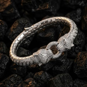 May include: A silver bracelet with two panther head clasps, adorned with sparkling stones. The bracelet's band has a textured, honeycomb pattern. The panther heads connect to form a clasp, creating a luxurious piece of jewellery.