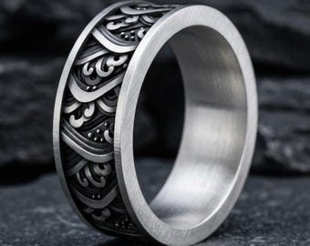 May include: A silver-toned metal ring featuring a wide band with a deeply engraved, repeating wave pattern. The exterior surface displays a high-contrast design with dark, recessed areas between the raised, polished silver wave motifs.