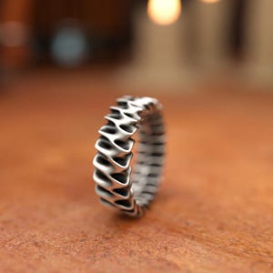 Unisex sterling silver band ring with geometric wave design captured in warm candlelight setting