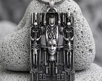 May include: A rectangular silver-toned pendant featuring a complex, biomechanical relief design. The center displays a human face surrounded by intricate mechanical structures, two skeletal figures, and a vertical arrangement of skulls.