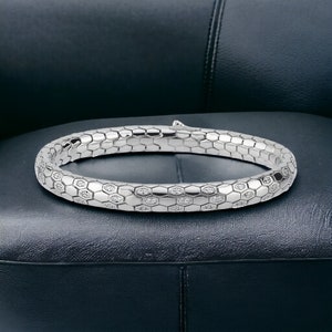 May include: A silver bangle bracelet with a textured honeycomb design and small clear stones set into the surface.