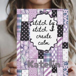 May include: A notebook with a patchwork design in shades of purple, white, and black. The cover features the text "stitch by stitch I create calm" in a decorative frame, and the name "Katelin" in a script font.