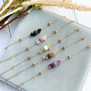 May include: Five gold chain bracelets with different coloured gemstone beads. Each bracelet has a lava rock bead and a variety of other beads, including pink, white, yellow, and purple.