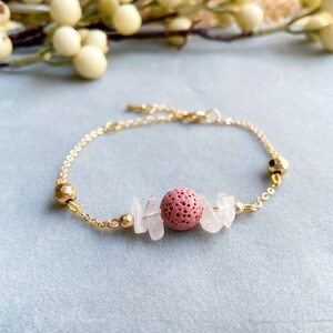 May include: A gold chain bracelet featuring a pink lava rock bead and clear quartz chips.