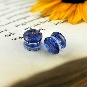 May include: A pair of blue glass ear gauges with white swirls. The gauges have a sparkly finish.