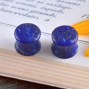 May include: Pair of blue lapis lazuli stone ear gauges. The gauges are round and have a speckled appearance.