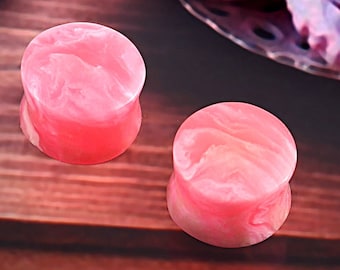 May include: Pair of pink and white marbled acrylic ear gauges. The gauges have a swirl pattern.