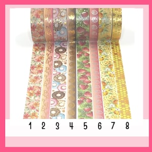 Könnte beinhalten: Acht Rollen dekoratives Washi-Tape mit verschiedenen Mustern, darunter Blumen, Donuts, Erdbeeren und Goldfolie. Das Band ist von 1 bis 8 nummeriert.