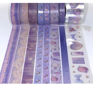 May include: A collection of decorative washi tapes in shades of purple, lavender, and silver. The tapes feature various designs, including celestial motifs, landscapes, and floral patterns. Some tapes have a holographic, glittery finish.