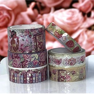 May include: Decorative washi tape rolls with floral, book, and strawberry designs. The tape features a variety of colors, including burgundy, gold, and pink. The rolls are stacked, showcasing the different patterns and themes.