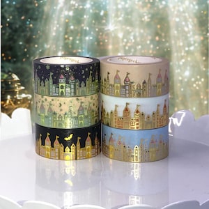 May include: A stack of decorative washi tape rolls featuring castle designs. The rolls display various colors, including black, beige, light blue, and gold, with the text "papergeek" visible on the top of each roll. The castle illustrations are detailed with gold accents.