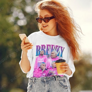 May include: White t-shirt with a graphic of a singer in a pink hoodie, the word "Breezy" in blue and purple, and the text "I Got Lucky". The shirt is worn by a person wearing sunglasses and jeans.