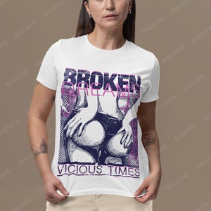 May include: White t-shirt with a graphic design featuring the text "BROKEN DREAMS" and "VICIOUS TIMES" in a distressed font. The design includes a stylized illustration in shades of purple and blue.