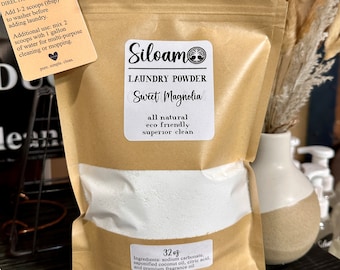 May include: A brown paper bag filled with white laundry powder. The bag has a label that says "Siloam Laundry Powder Sweet Magnolia all natural eco friendly superior clean" and "32 oz Ingredients: sodium carbonate, saponified coconut oil, citric acid, and premium fragrance oil".