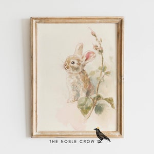 May include: A framed watercolor painting of a brown rabbit with pink ears sitting on a green leafy branch with pink flowers. The painting is in a light wood frame with a white mat.