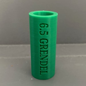 Pode incluir: Um cilindro de plástico verde com o texto "6.5 GRENDEL" gravado no lado.
